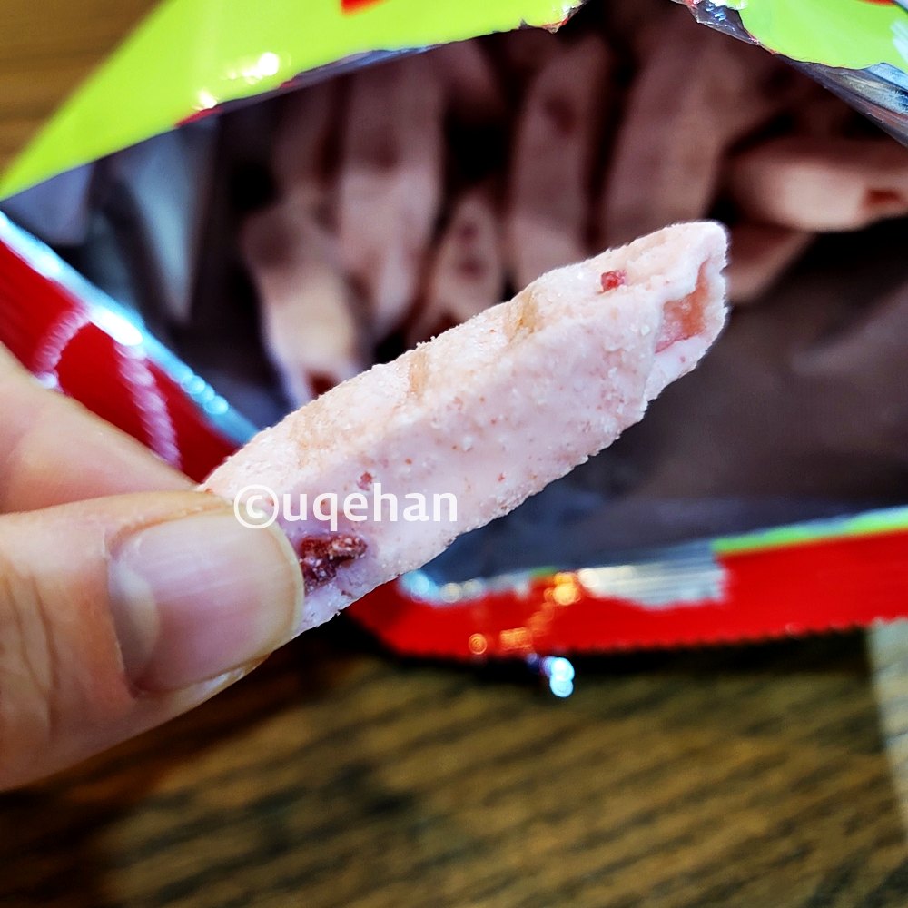 오리온 오! 딸기 과자를 손으로 잡고 있따. 긴 막대기에 가운데가 뚫려있따. 과자 중간에 분홍색 딸기 쿠키가 부서져 붙어있다.