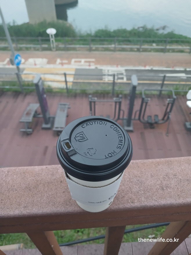 야외 운동기구 옆 난간 위에 놓인 테이크아웃 블랙커피 컵