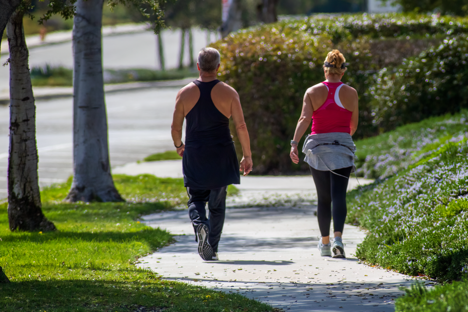A couple walking along a sunny park pathway, enjoying outdoor exercise.
