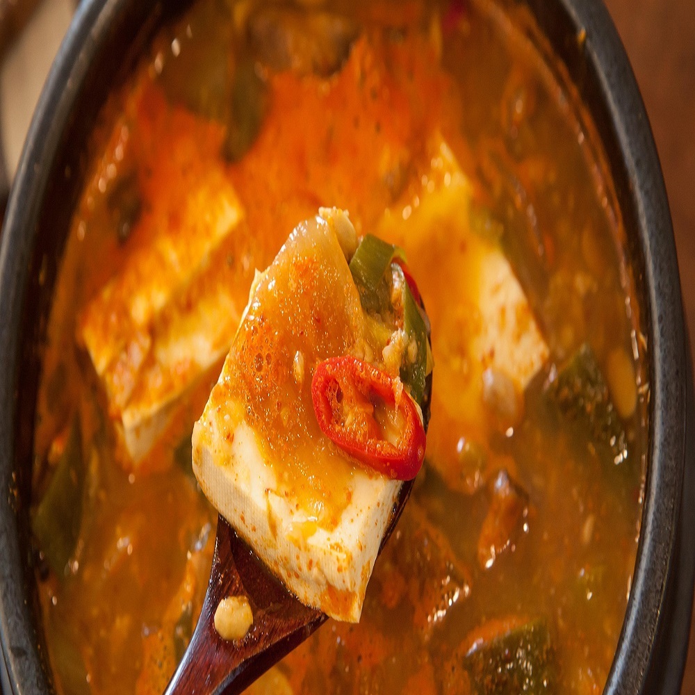 뚝배기에서 갓 끓여낸 된장찌개와 숟가락 위에 올려진 부드러운 두부와 고추 고명