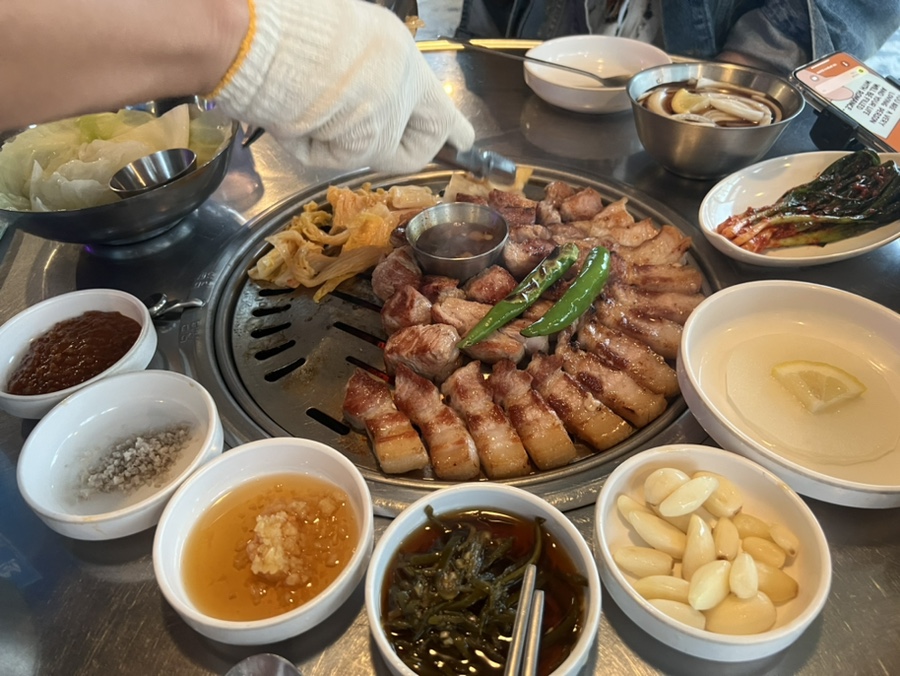 기장 삼겹살 맛집 부산댁의 메인 삼겹살과 푸짐하게 차려진 한 상 차림, 고기와 반찬이 풍성하게 구성된 모습