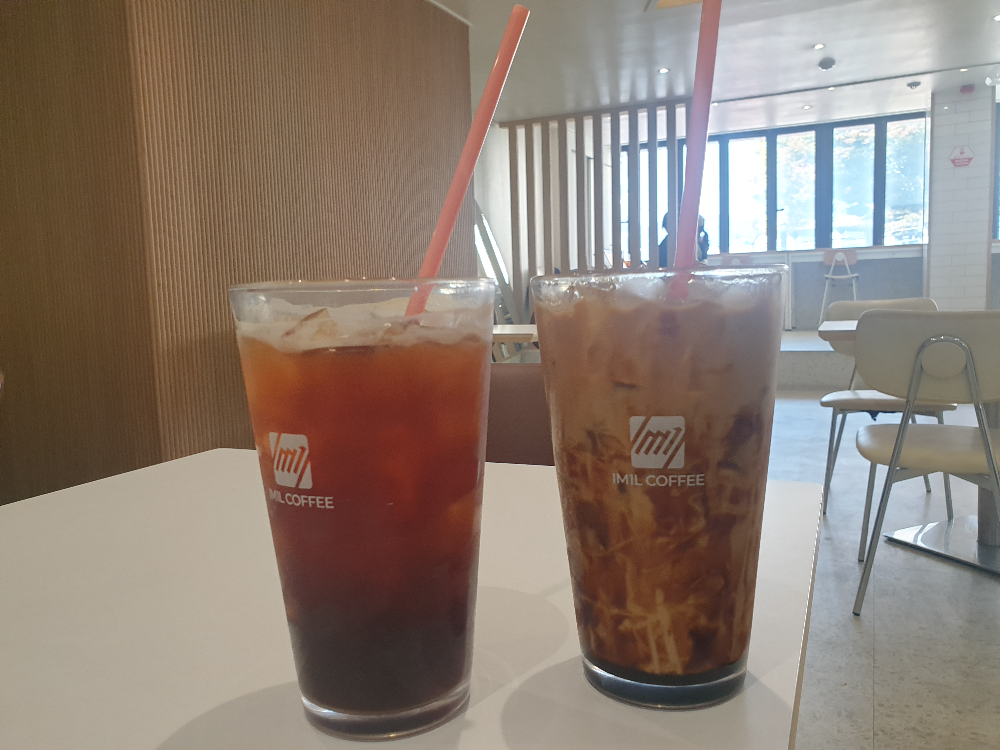 흰 색 테이블 위에 커피컵이 위에 올려져 있다. 컵에는 빨대가 꽃혀있다.