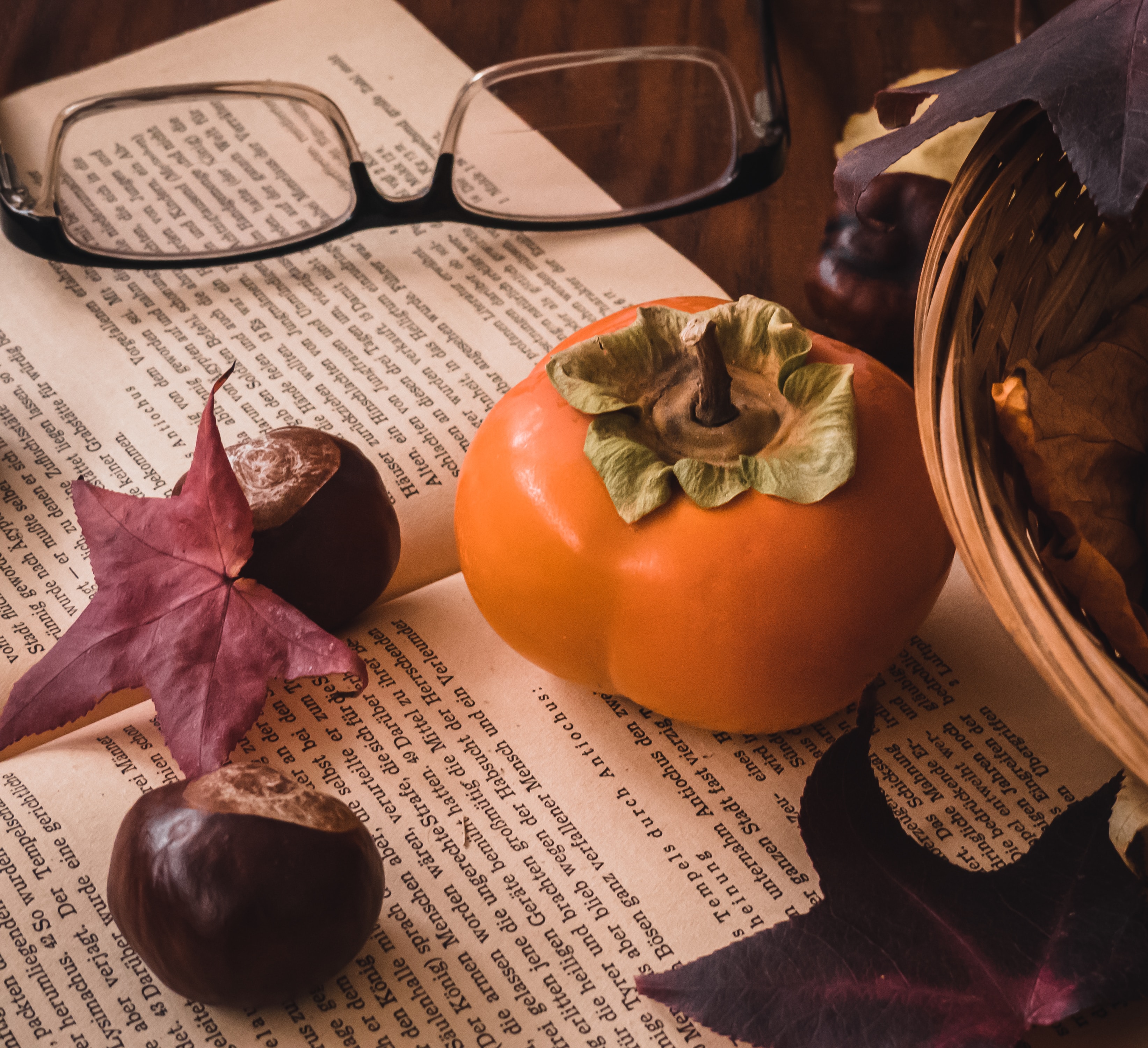 영문 책 위에 올려진 검정 안경과 단감 한 개가 올려져 있다. 단감은 주황색으로 단단하게 생겼다.