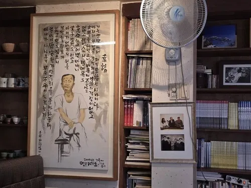 손글씨 시와 함께 표구된 천상병 시인의 초상화, 흑백사진과 오래된 책이 꽂힌 책장