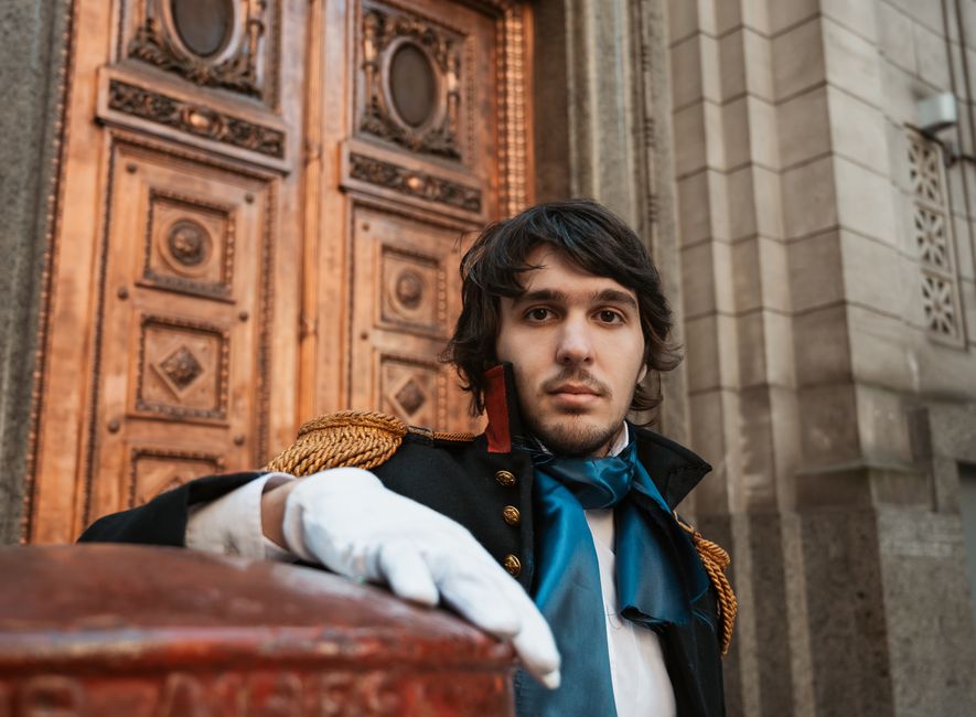Man in historical attire poses by ornate doors in Buenos Aires.