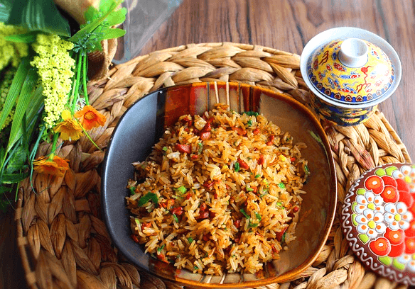 넓은 접시에 볶은밥이 가득하다. 연갈색으로 야채와 햄조각들이 있다.