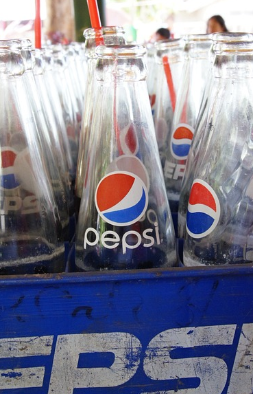 Many empty bottles of Pepsi Cola inside a plastic box.