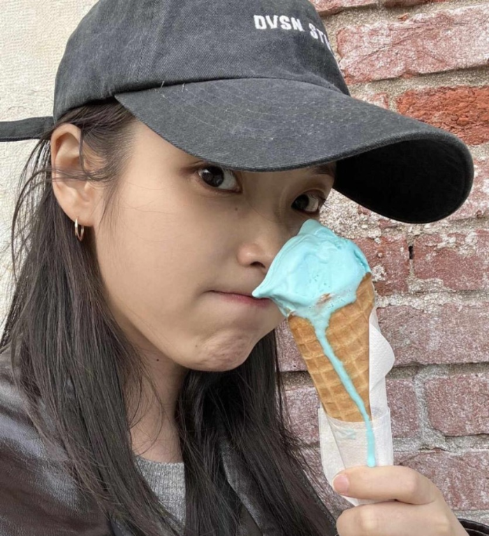 챙이 있는 검은색 모자를 쓰고 녹아내리는 민트초코 아이스크림을 먹으며 입을 꾹 다물려 귀여운 표정을 짓는 아이유