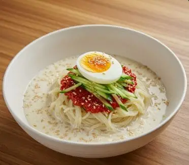 콩국물 위에 소면과 양념장, 오이채, 삶은 달걀이 올라간 콩국수 한 그릇. 참깨가 고명으로 뿌려져 있다.