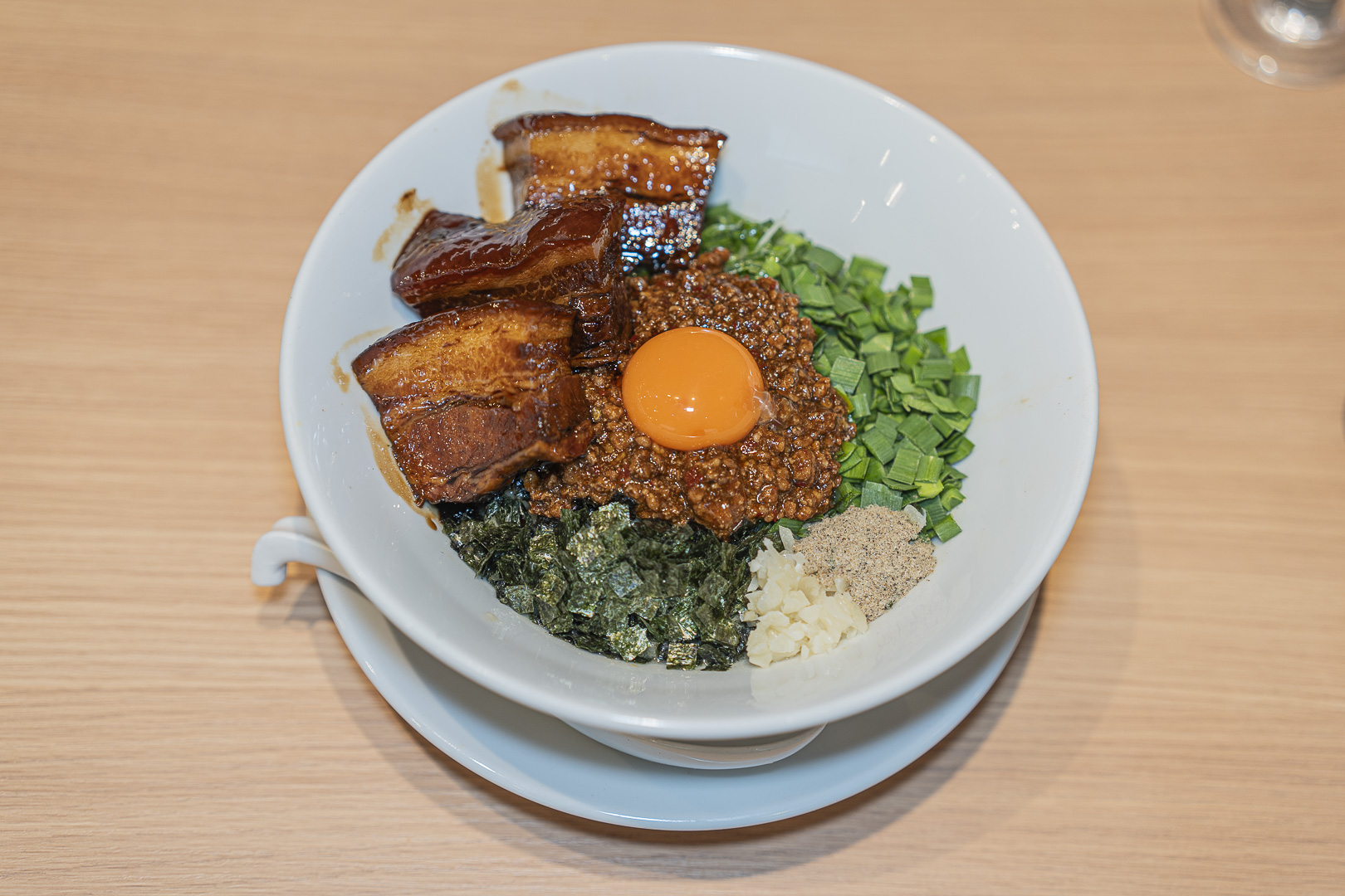 Notenki: a white bowl of mixed noodles topped with egg yolk, thick meat, minced meat, nori and garlic chives.
