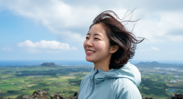 제주도의 오름 정상에서 바람을 맞으며 풍경을 바라보는 여행자