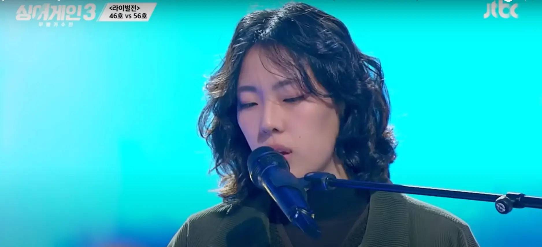 싱어게인 3- 초록색 자켓을 입고 곱슬단발머리로 스탠딩마이크앞에서 노래하는 56호 상반신