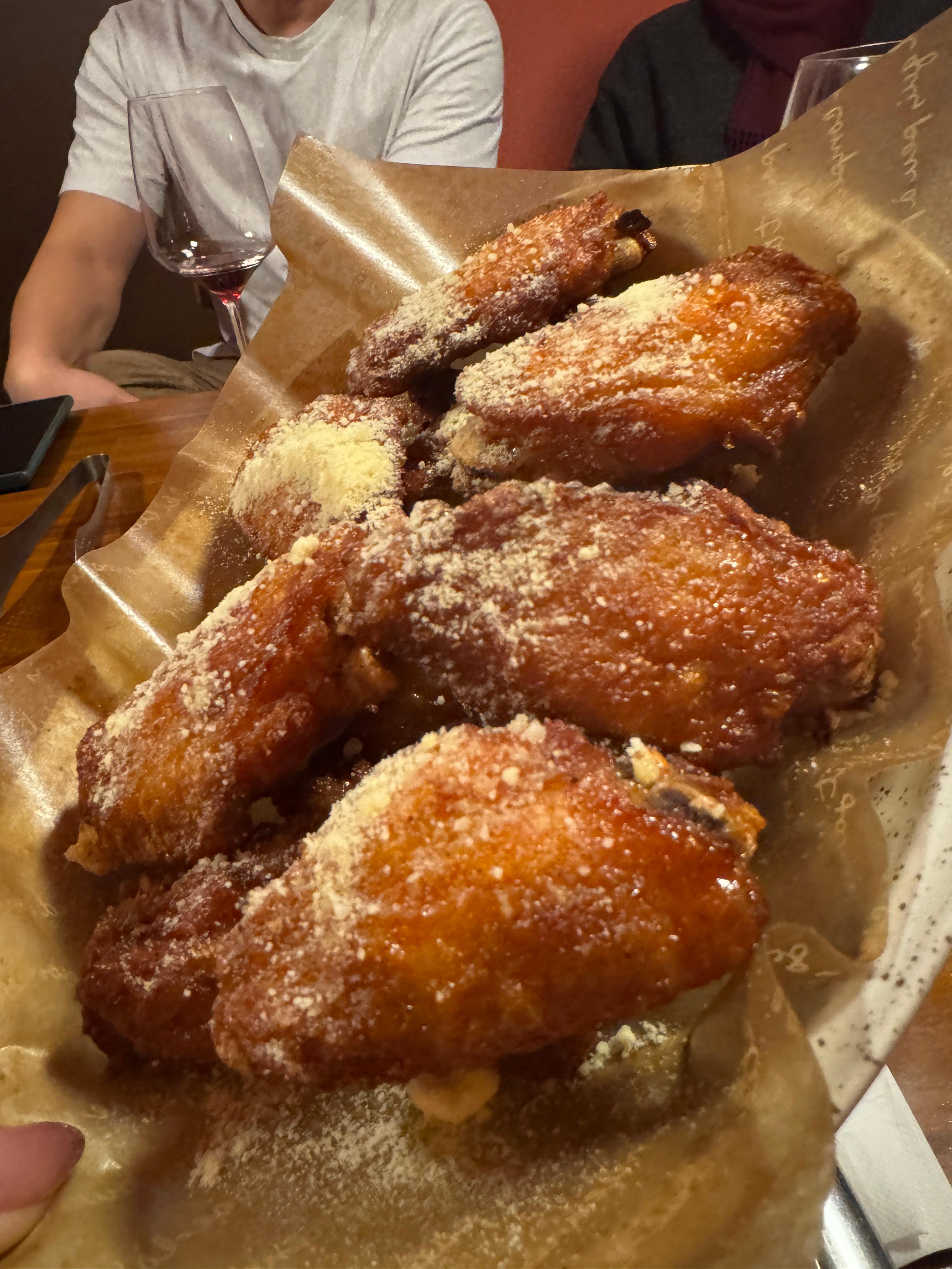 종이 위에 담긴 치킨윙 한 접시&amp;#44; 주황빛 소스가 입혀지고 위에 치즈 가루가 듬뿍 뿌려진 와인 안주