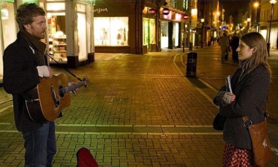 영화 원스의 한장면으로 기타를 든 남자와 가방을 멘 여자가 서로 바라 보고 있습니다.