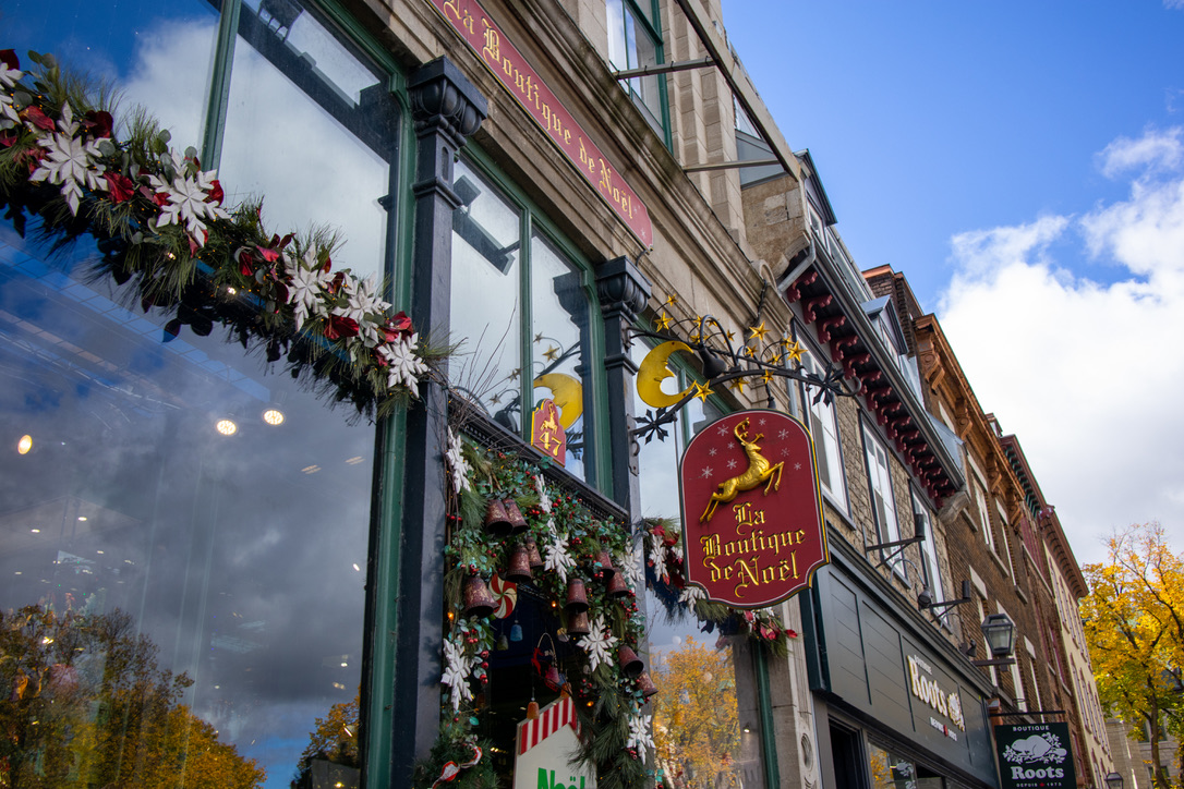 La Boutique de Noel의 외부 사진. 겉에는 창틀을 따라 크리스마스 장식품들로 꾸며져 있고 유리창으로는 안이 들여다보인다. 노엘 부티크의 장식이 보인다. 전반적으로 빨간색 배경에, 금색 사슴과 금색 필기체 글씨로 La Boutique de Noel이라고 적혀있다.