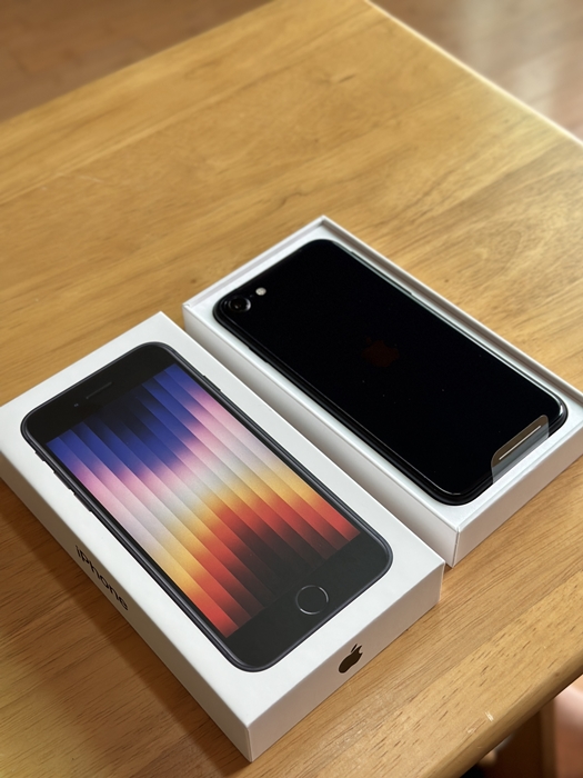아이폰 SE3 256GB 본체와 박스, 나무 테이블 위에 박스를 열어 본체 뒷면과 전면 패키지가 함께 보이는 모습
