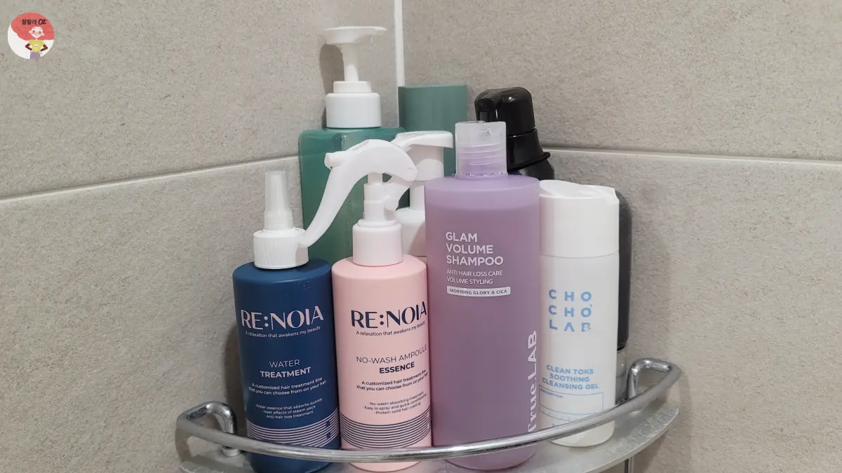 욕실 선반에 헤어&middot;스킨케어 제품들이 정리된 모습. 파란색 RE:NOIA 워터 트리트먼트, 분홍색 노워시 앰플 에센스, 보라색 True LAB 샴푸, 흰색 CHOCHO LAB 클렌징 젤 등이 보인다.