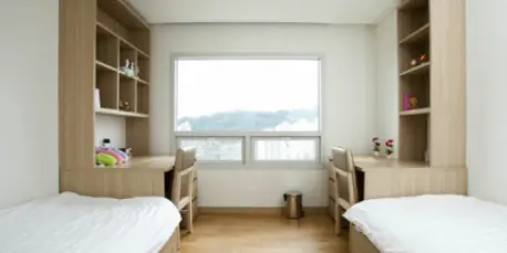 재수학원- 흰색 기숙사안 양쪽벽면 흰색 침대 끝부분 책장 일체형 책상과 의자