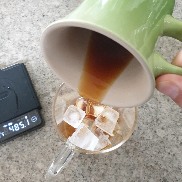 초록색 커피잔 속에 있는 커피를 얼음이 담긴 유리컵에 붓는다.