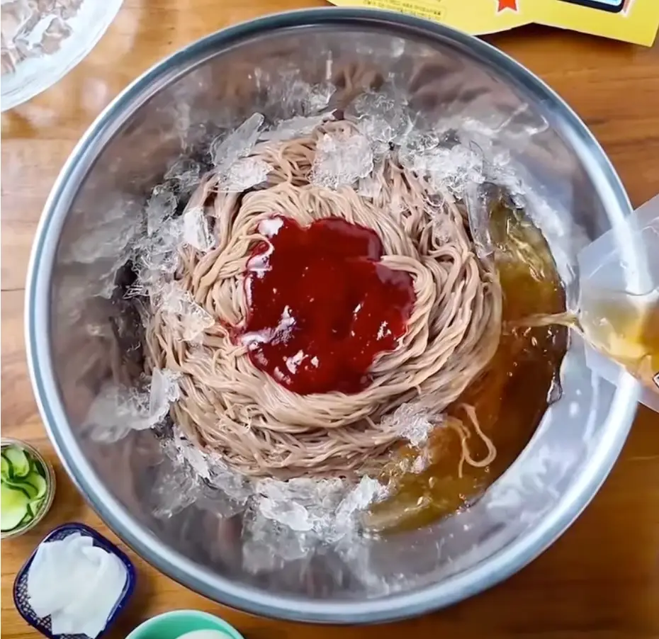 스테인레스 용기안 냉면 위 빨간 양념에 육수를 붓는 이미지