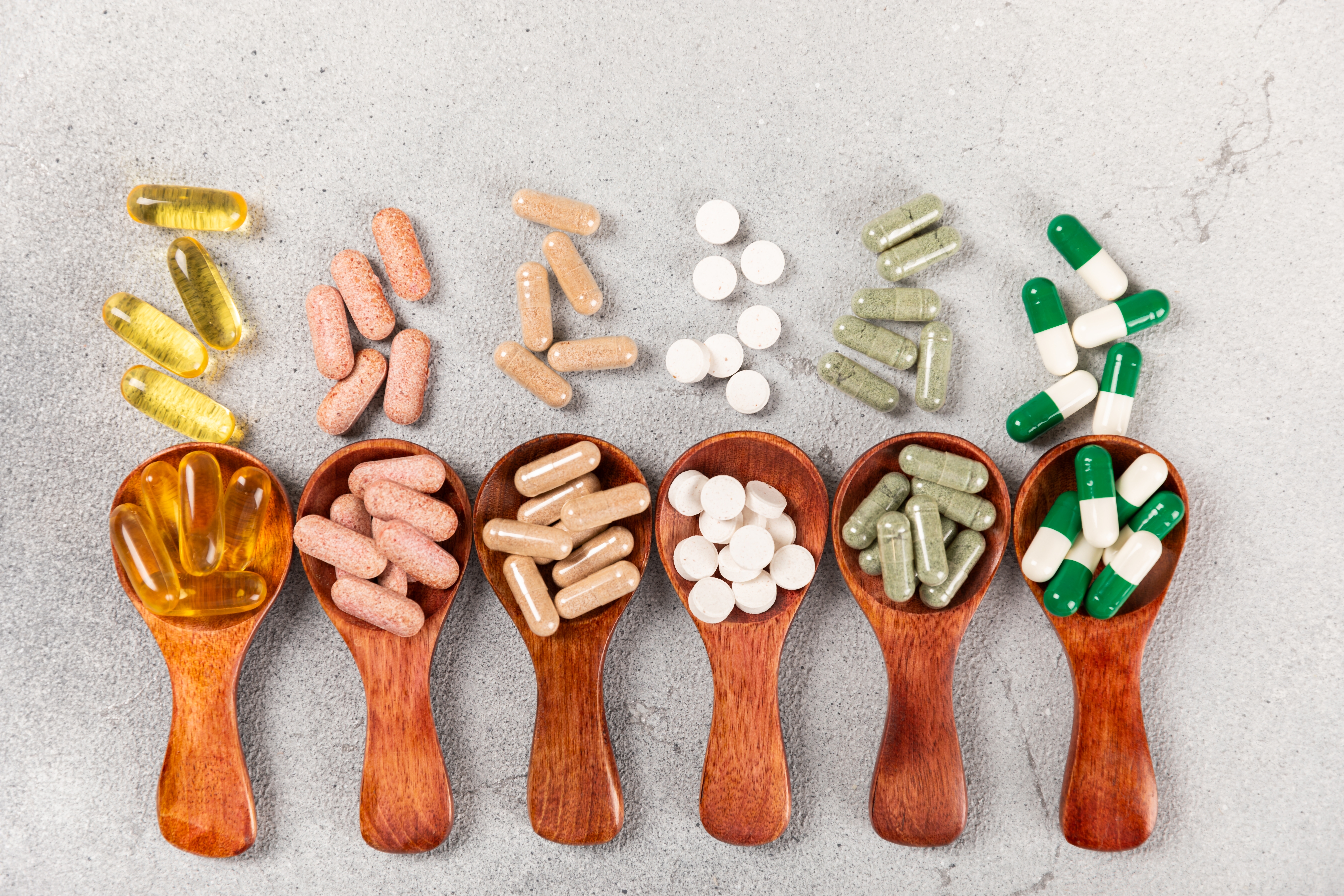 다양한 색상과 형태의 건강기능식품 보조제를 나무 숟가락 위에 담은 이미지