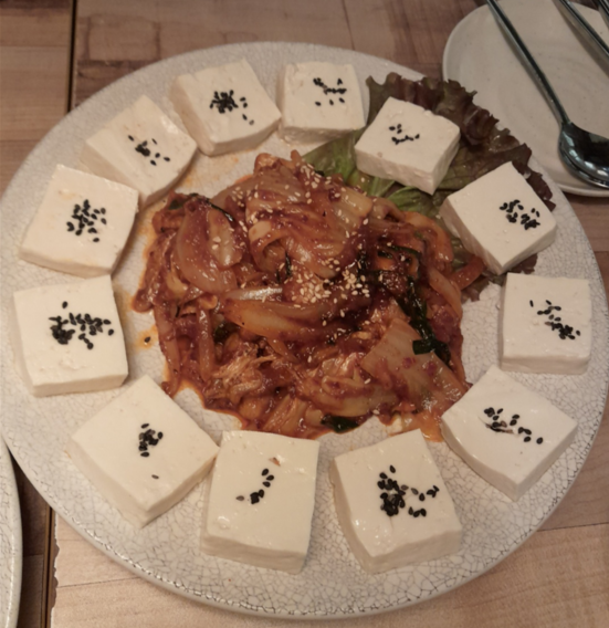 접시에 두부김치가 올려져 있다. 두무가 빙 둘러져 있고 가운데에 볶음 김치와 약간의 고기가 올려져 있다.