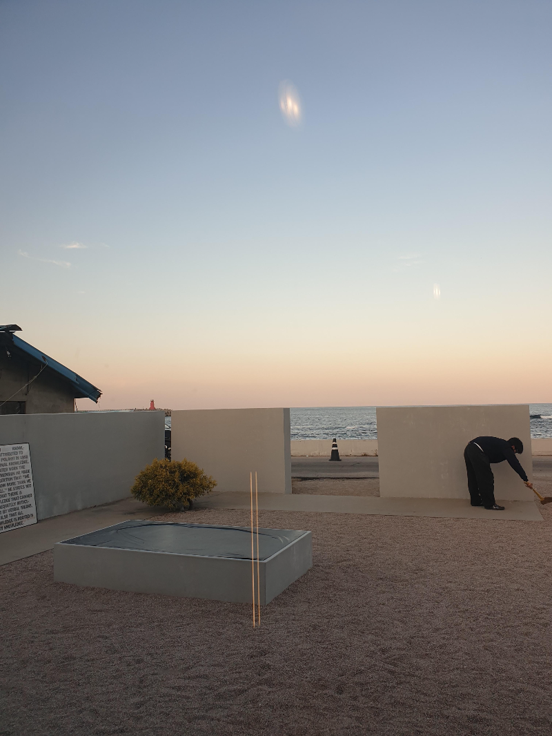 담 사이로 보이는 바다. 담 아래를 청소하는 직원이 보인다.