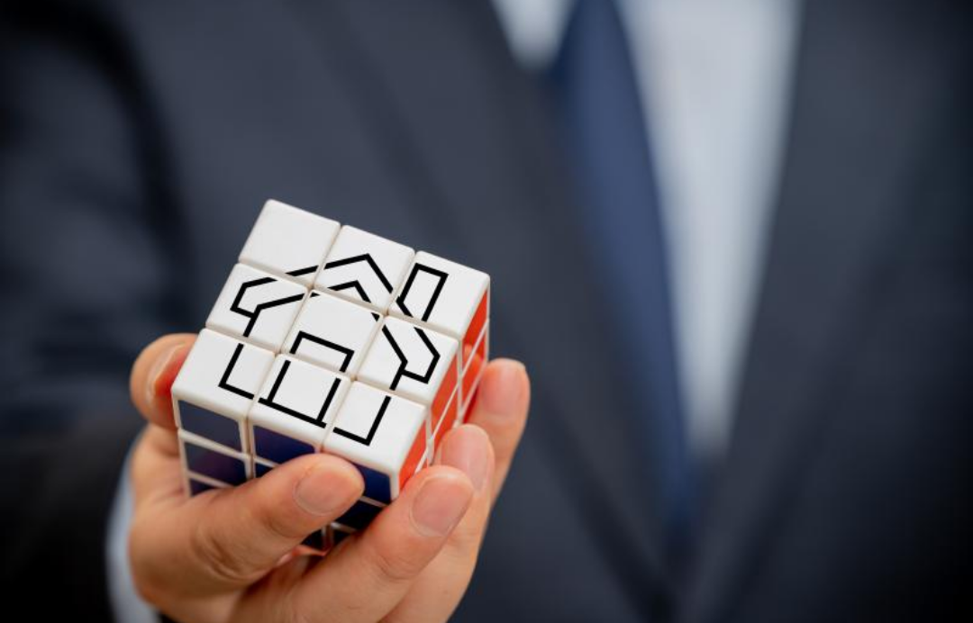 한 남자가 집그림이 그려져있는 큐브를 들고 있다.