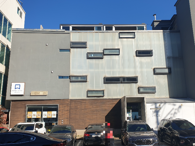 1층 적벽돌, 2,3층은 회색으로 된 건물. 주차장에는 차들이 세워져있다.