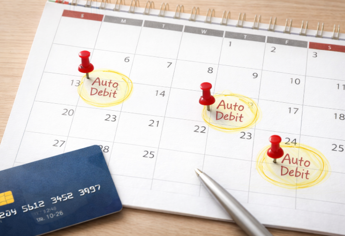 달력에 자동이체 날짜가 표시되어 있고 신용카드와 펜이 놓여 있는 장면으로, 반복되는 고정 지출 구조를 상징하는 이미지