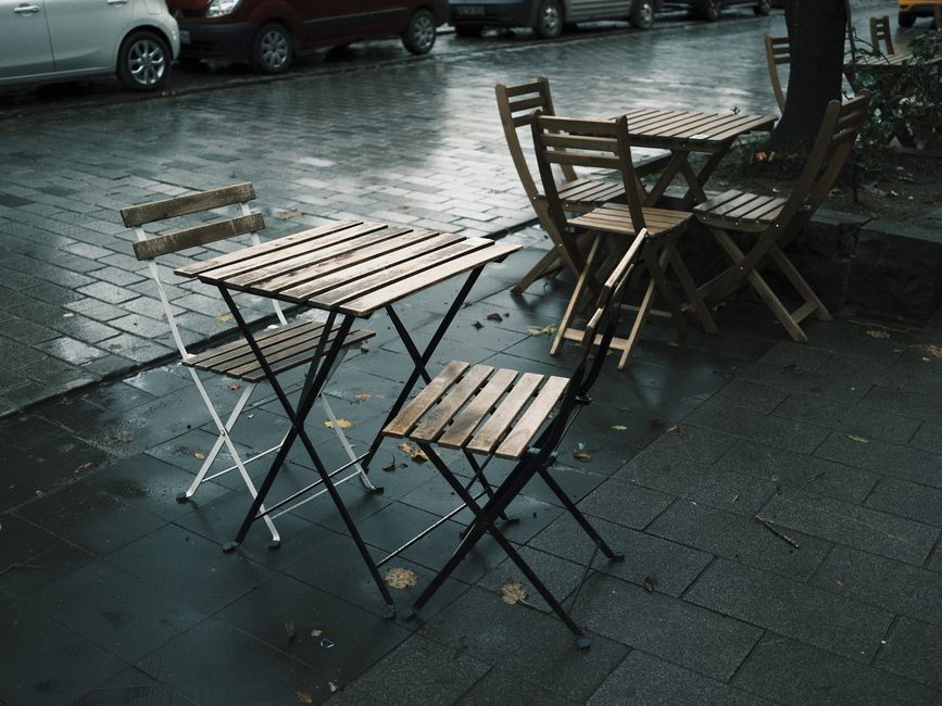 Empty wooden caf&eacute; tables and chairs on a rainy street, evoking a nostalgic mood.