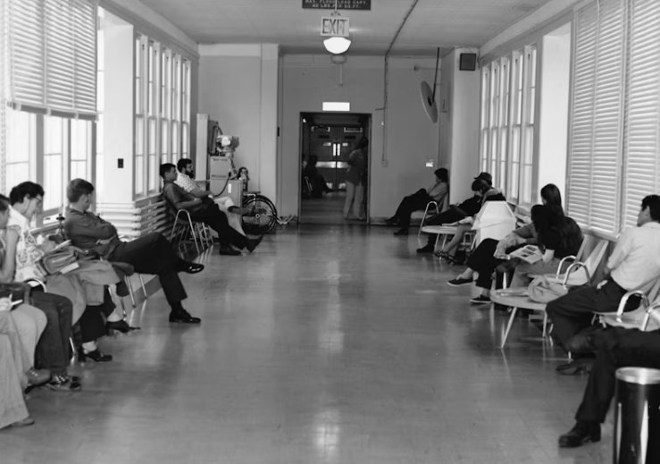 병원 복도에 환자들이 앉아 대기하고 있는 흑백 사진, 겨울철 병원비 증가를 상징하는 장면