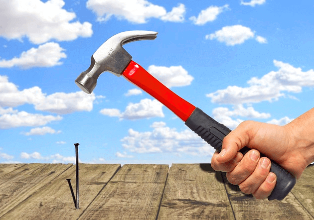 빨간 손잡이를 가진 쇠망치가 못을 박기 위해 허공에 있다.