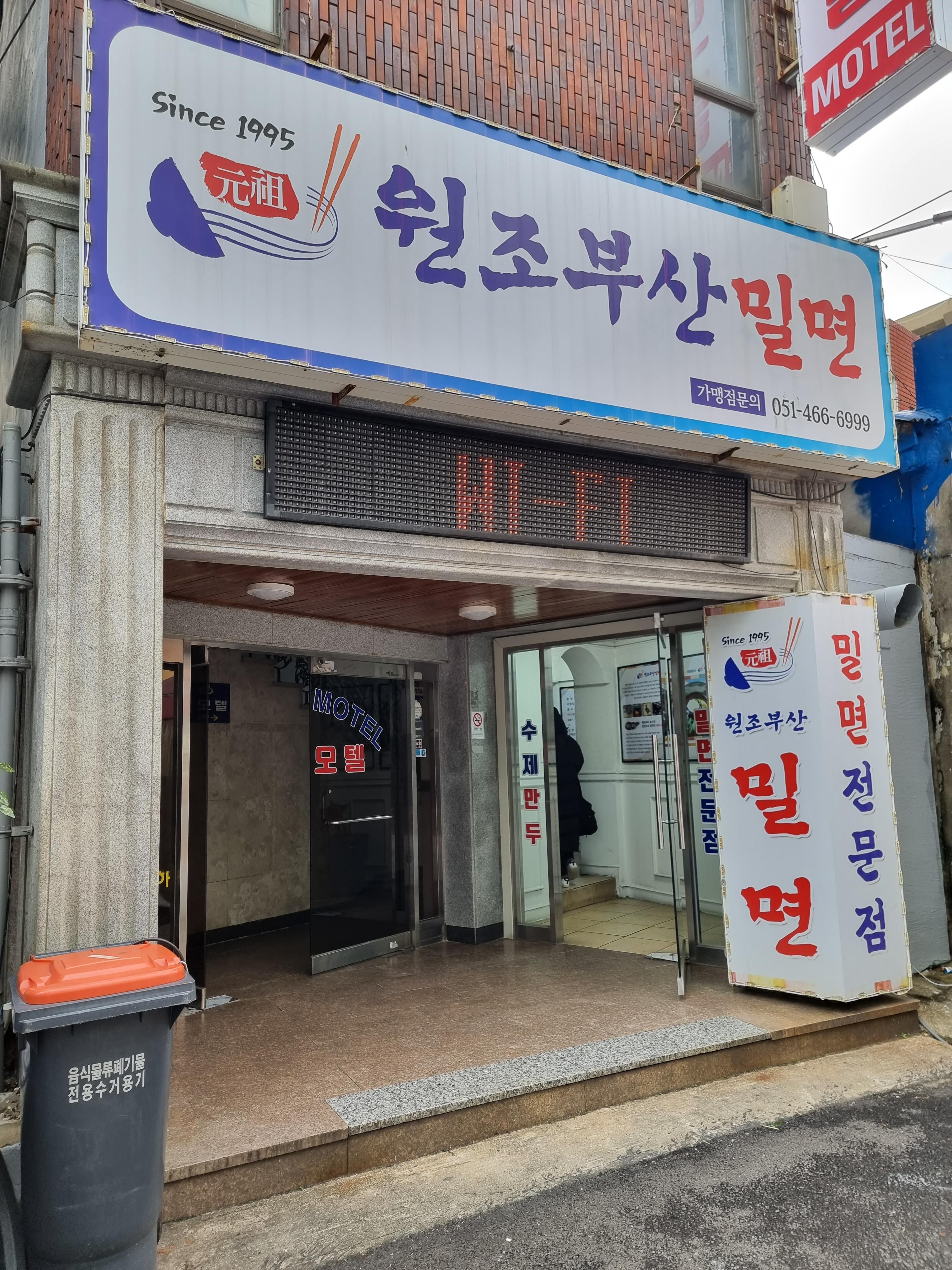 시장 입구 하나은행 옆, 도보 1분 거리에 위치한 '원조부산밀면'의 간판입니다.