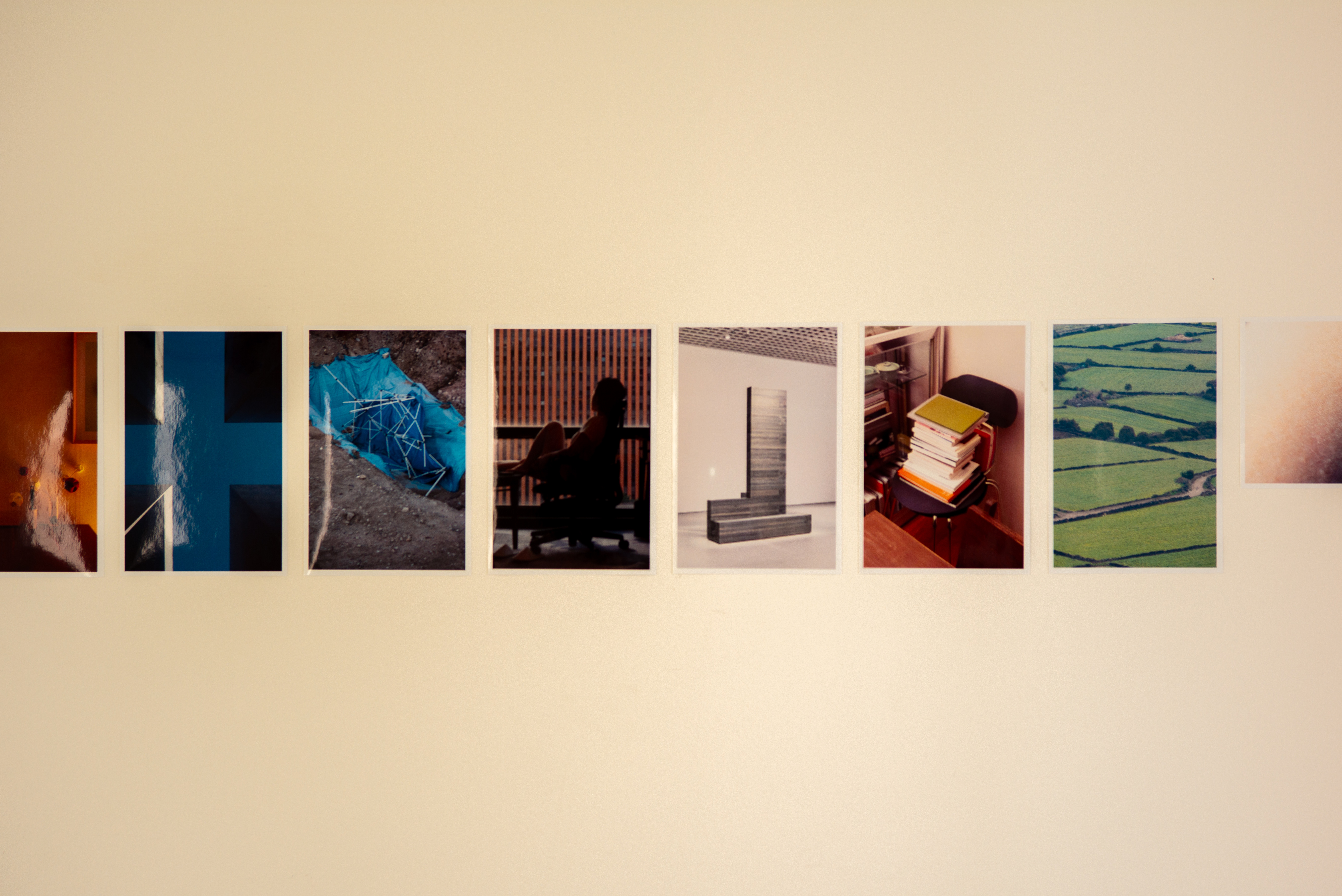 실내 조명을 받아 미색(ivory)으로 표현된 벽면에 여러 장의 사진 인화물이 일렬로 붙어 있는 모습