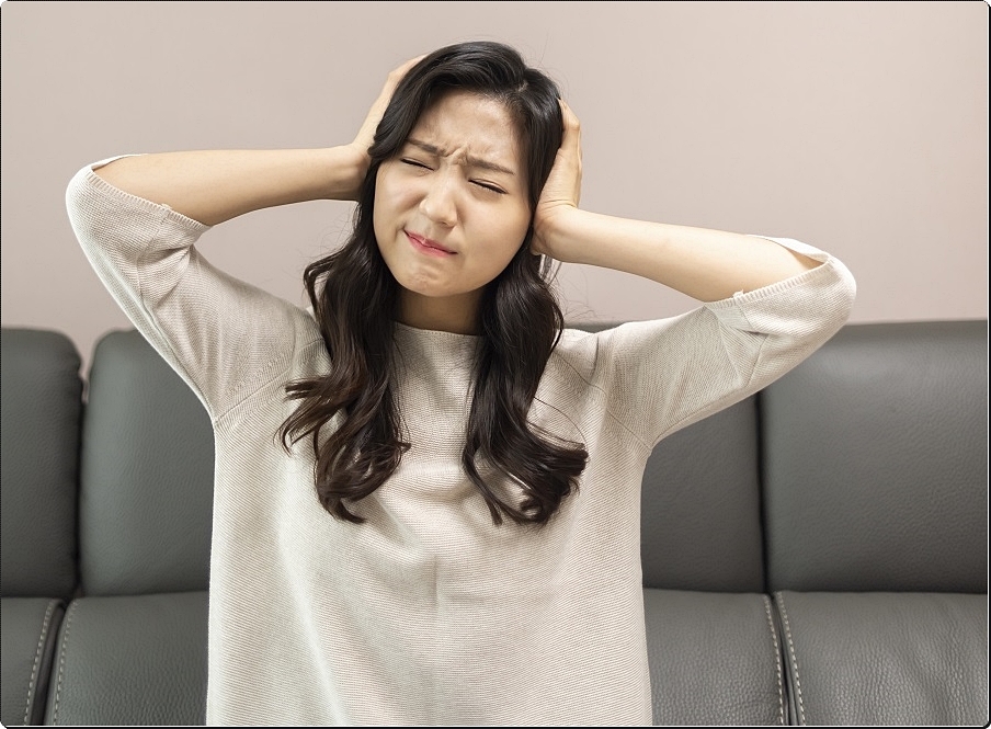 양쪽 귀를 손바닥으로 막고 괴로운 표정을 짓고 있는 여성의 모습
