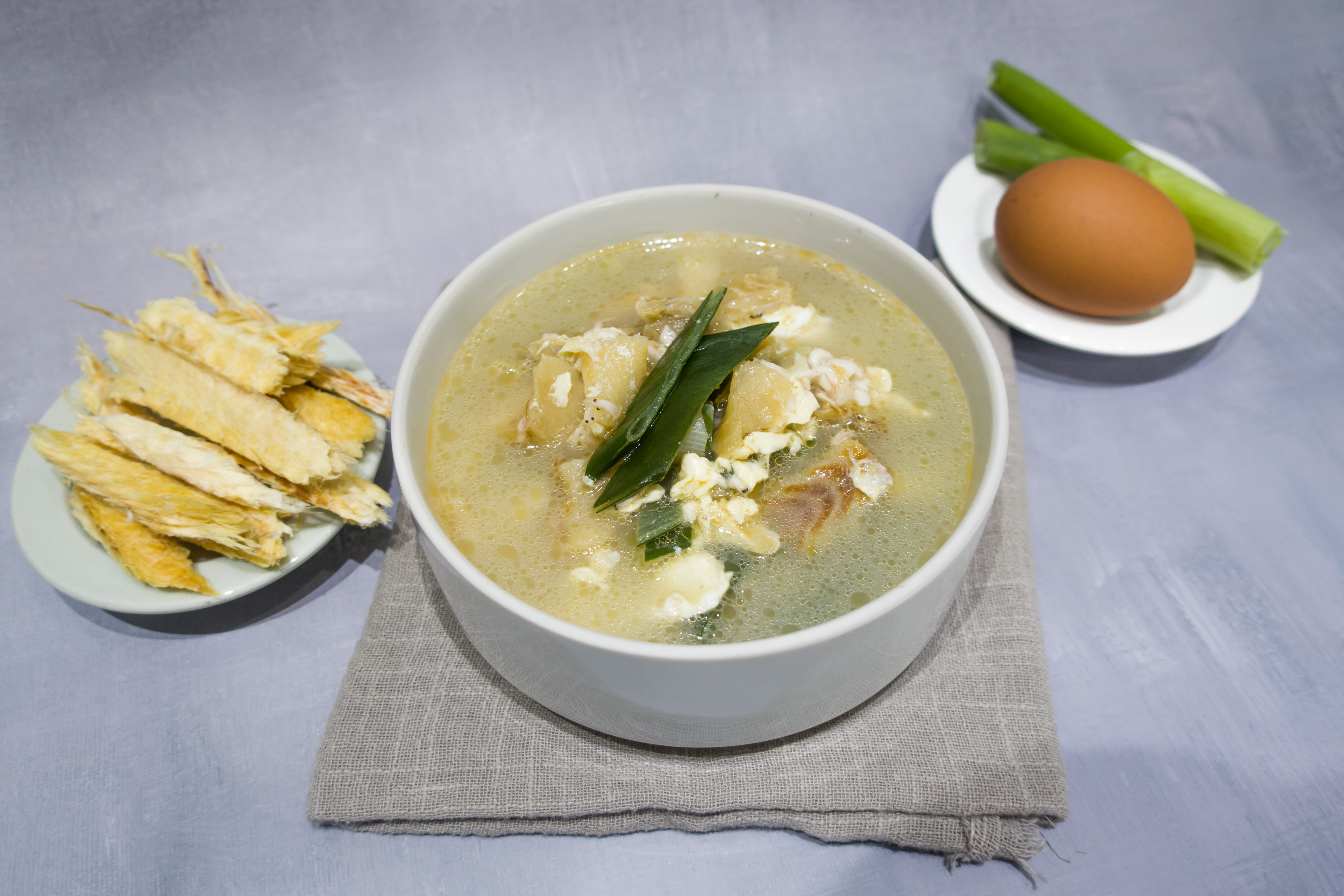 가운데 흰 그릇에 북어와 계란&#44; 파 등을 넣고 끓인 북어국을 놓고&#44; 왼쪽에는 흰 접시 위에 찢어 놓은 북어를 놓았고&#44; 오른쪽에는 흰 접시 위에 계란과 파 조각을 둔 사진