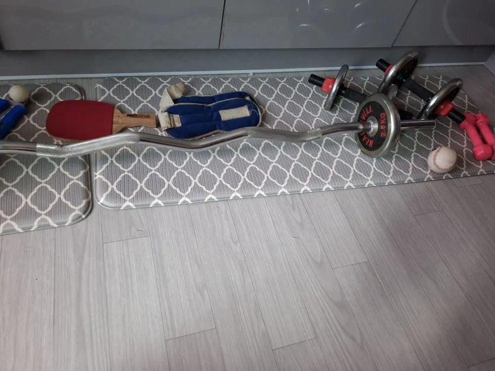 거실 매트 위에 놓인 EZ컬바, 조립식 덤벨, 아령, 악력기, 탁구채 등 다양한 운동기구.
