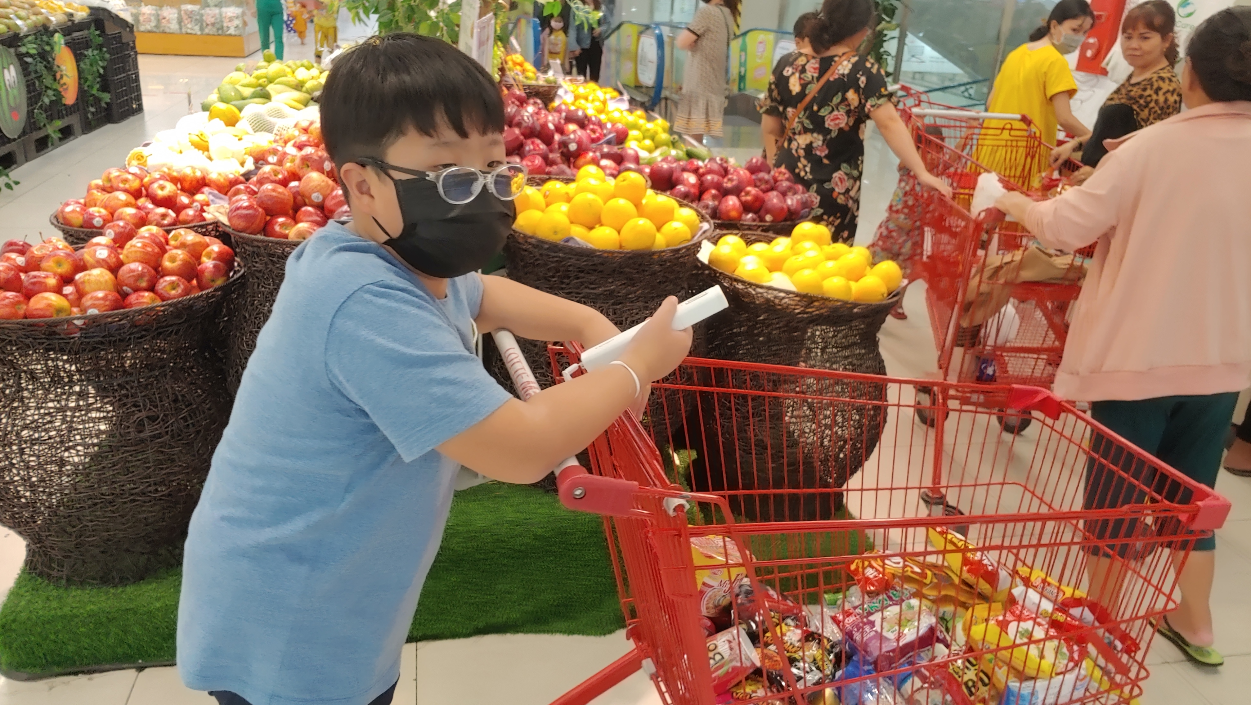 쇼핑카트를 미는 똘망이. 카트에는 과자와 음식이 들어있고 옆에는 과일 진열대가 있다.