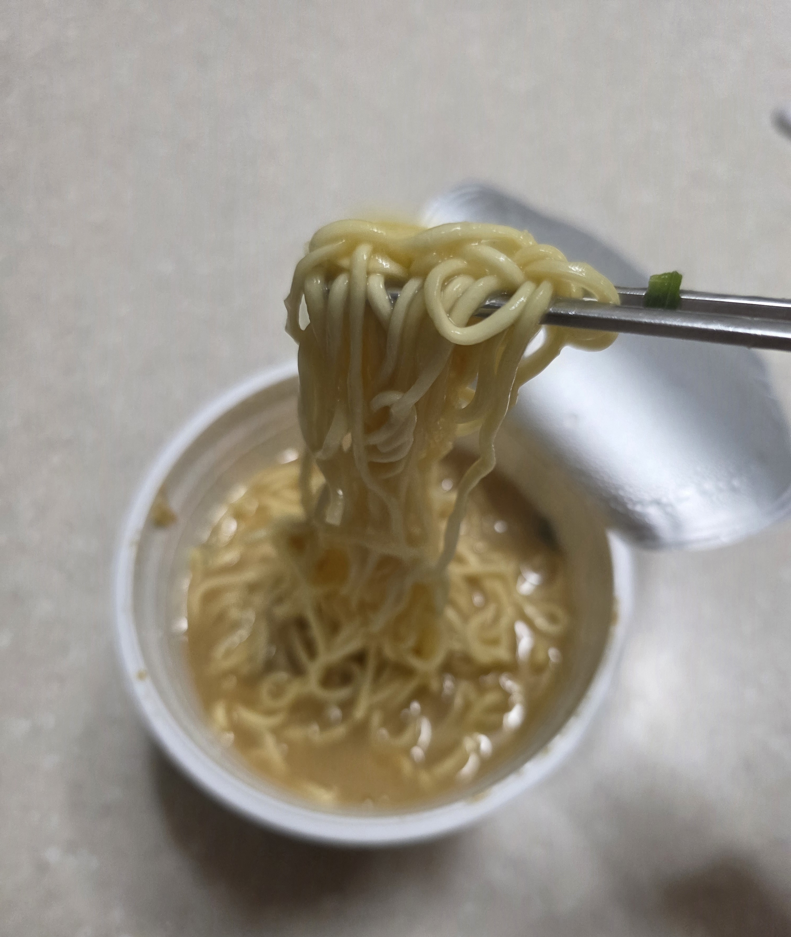 젓가락으로 들어 올린 텐카잇핀 컵라면의 노란 면발과 국물