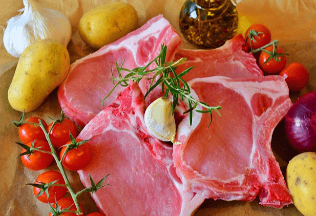 분홍색 돼지고기들이 가득하고 방울토마토와 감자, 통마늘, 적색 양파가 있다.