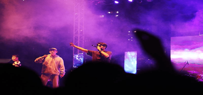 보라색 조명 속에서 래퍼들이 무대에서 열정적으로 공연 중인 모습