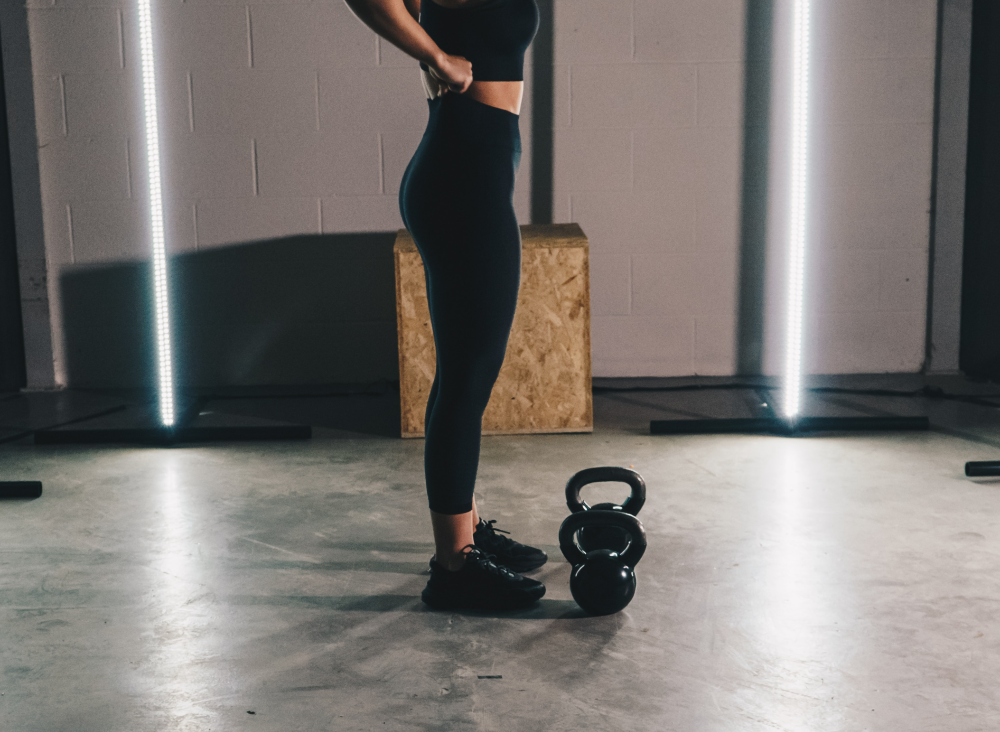 검은 케틀벨 두 개를 앞에 두고 레깅스를 정돈하는 여자