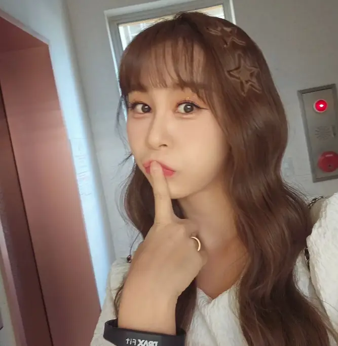 현역가왕- 갈색 웨이브 긴머리 흰색 원피스를 입고 오른손 검지손가락으로 입을 가리며 귀여운 표정을 짓는 윤태화