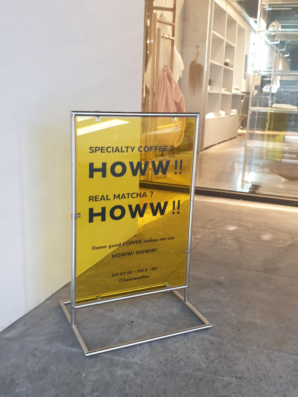 유리문 앞에 노란색 입간판. HOWW!! 스페셜티 커피와 말차가 강조되어 있다.