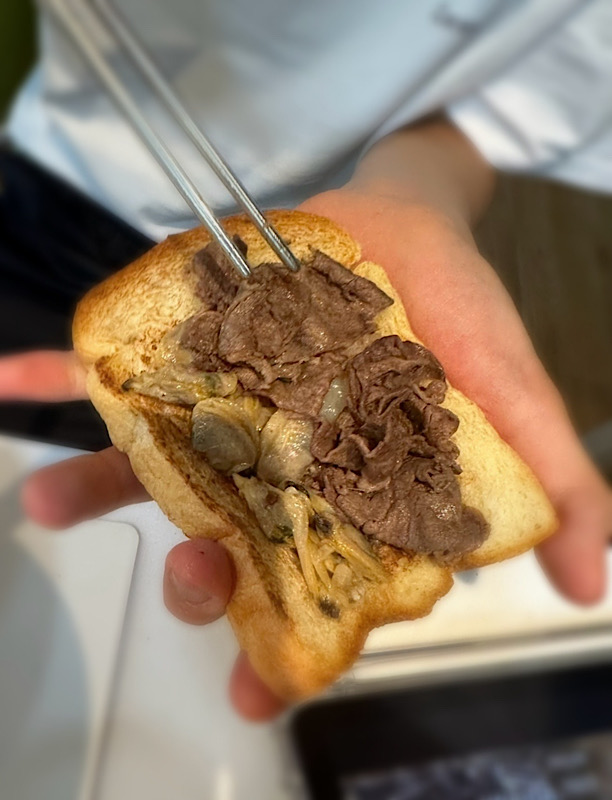 아이가 손바닥위에 구운 식빵위에 구운 소고기 바지락을 잔뜩 올려 오픈 샌드위치를 만드는 모습