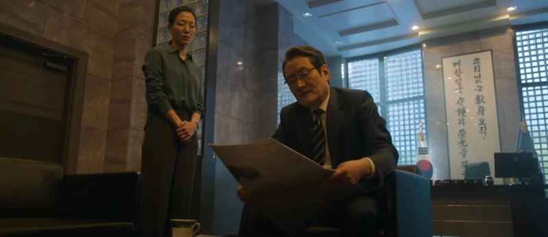 국정원 사무실 소파에 신문을 보고 있는 드라마 무빙의 민용준과 옆에 서 있는 여운규