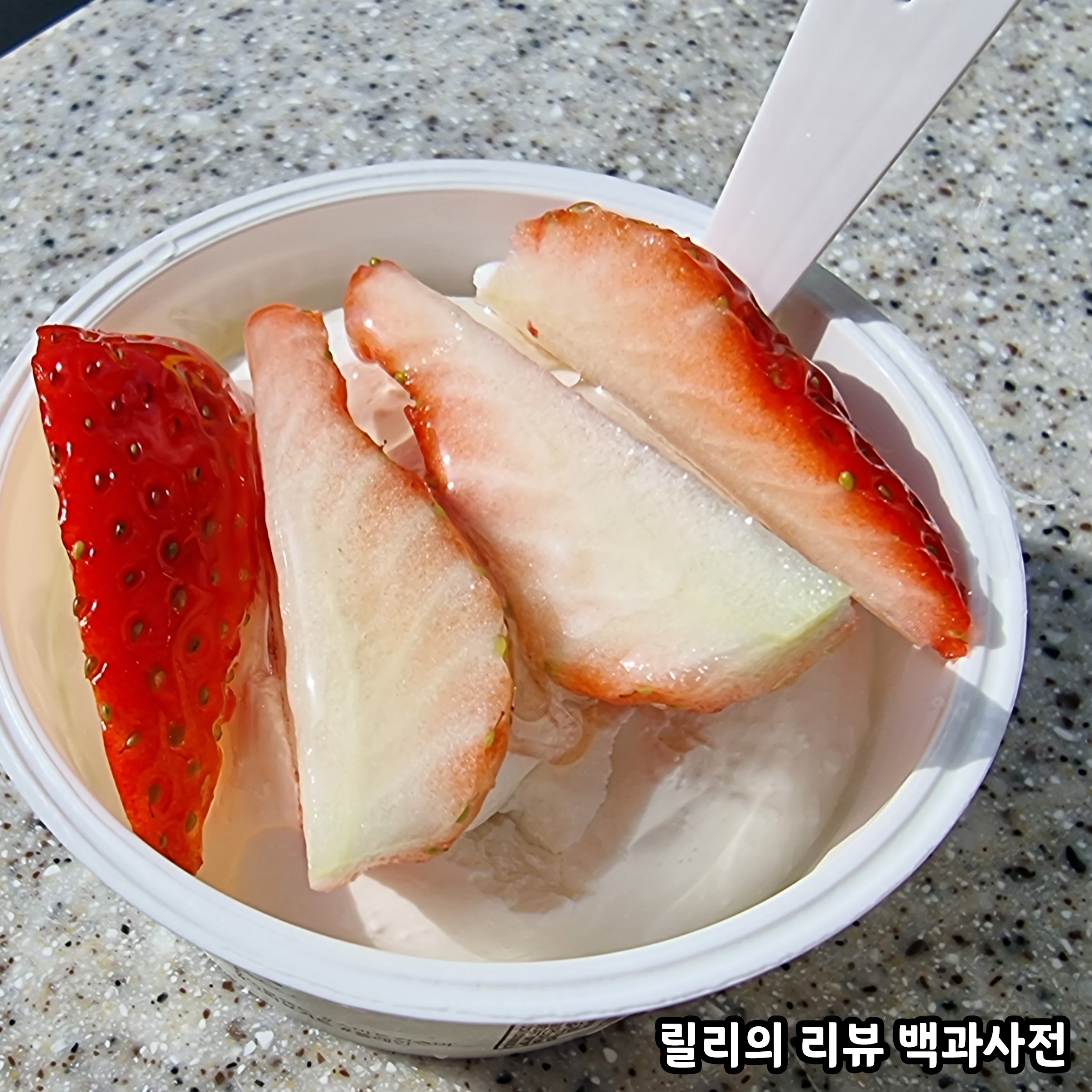 그릭요거트 위에 세로로 4등분 된 딸기를 올리고 그 위에 꿀을 뿌린 완성된 사진