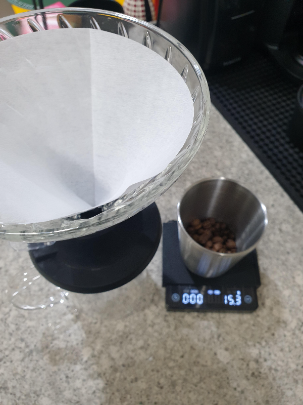 테이블 위에 필터가 꽃힌 하리우 스위치 드리퍼와 15.3g 원두가 담긴 컵이 올려져 있는 저울이 있다.