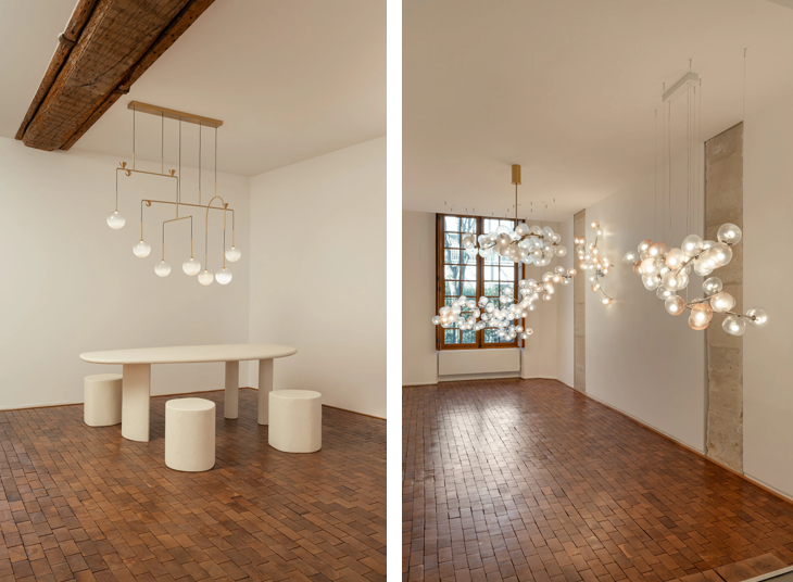 "Giopato & Coombes 파리 갤러리 전시 조명, 모빌 형태의 브라스 골드 조명과 구 형태의 감성 유리 조명이 어우러진 미니멀 인테리어 공간"